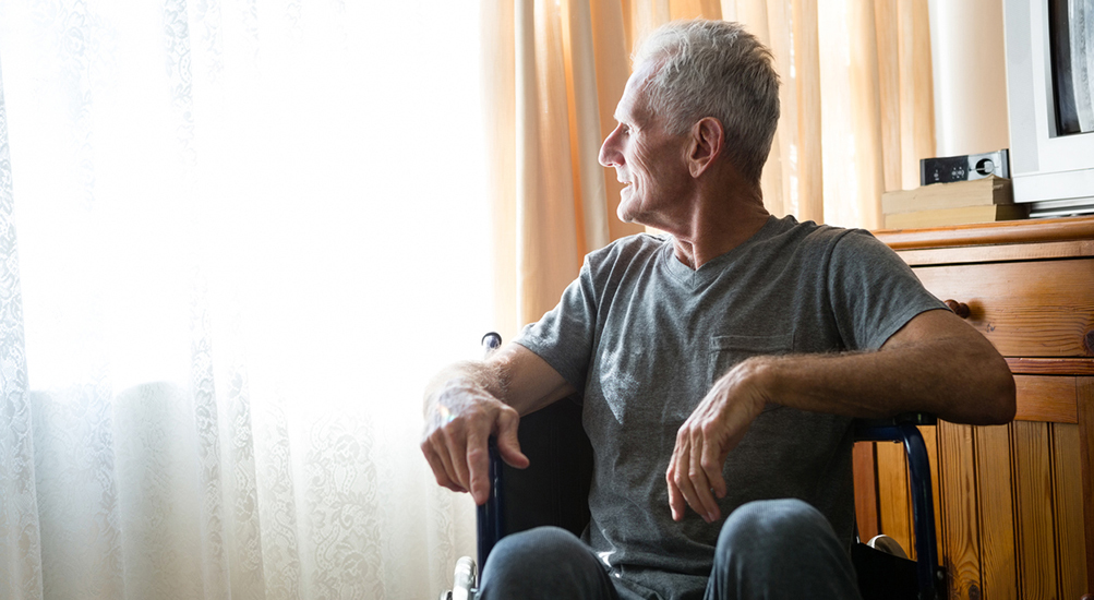 sad older man in a wheelchair looking out a window